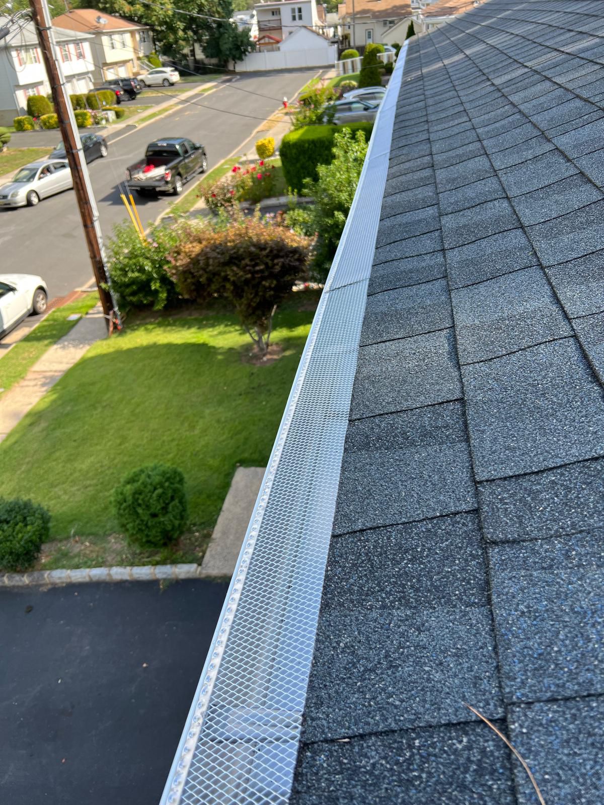 Long run of seamless gutter with leaf guard alongside a shingle roof